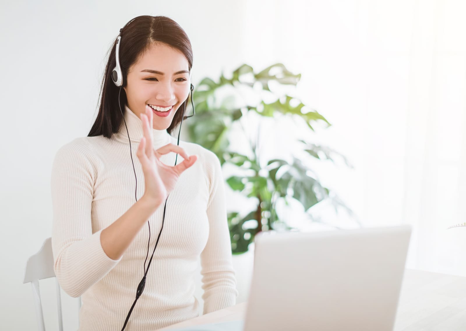 Young woman working on laptop and using video call in living room at home